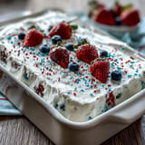 Colorful patriotic poke cake piled high with fluffy whipped topping and sprinkles.