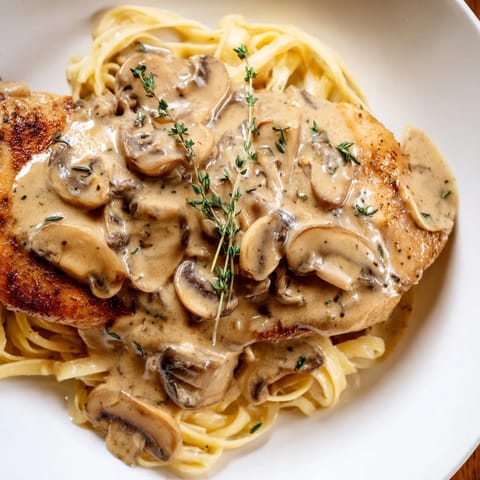 Close-up of tender Creamy Chicken Marsala with a rich, velvety mushroom sauce clinging to the pasta, topped with a sprinkle of Parmesan cheese.  