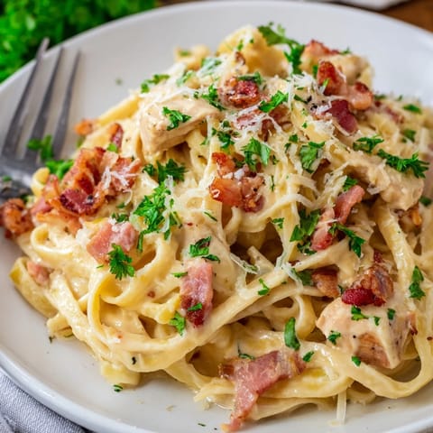 A close-up of Chicken Carbonara twirled on a fork, showcasing tender chicken and freshly cracked black pepper.  
