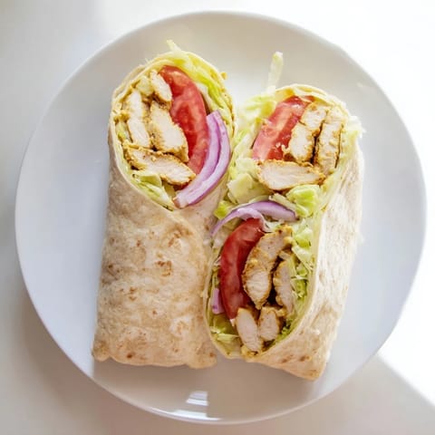 A close-up view of a sliced Honey Mustard Chicken Wrap, revealing juicy chicken, fresh vegetables, and creamy dressing inside the toasted tortilla.