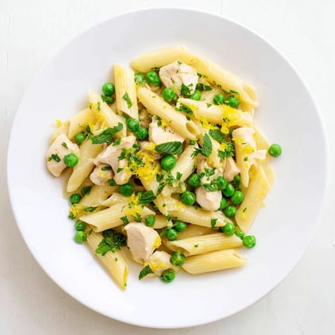 A close-up of Pea & Mint Chicken Pasta on a white plate, garnished with fresh herbs and freshly grated Parmesan.