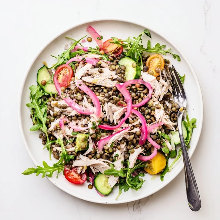 Served Lentil & Chicken Spring Salad on a white plate, with lentils, chicken, arugula, and pickled onions tossed in dressing.