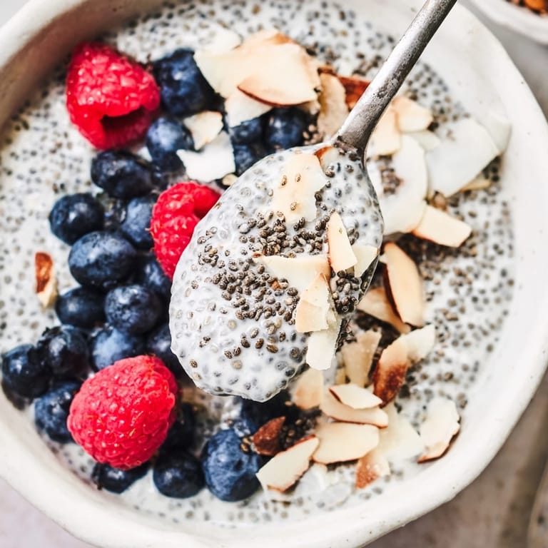 Healthy Poppy Seed Chia Pudding breakfast in a bowl with raspberries, coconut flakes, and a wooden spoon.