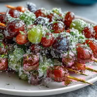 Frozen grape skewers with lime sugar glisten on a parchment-lined tray, juicy grapes coated in tangy lime zest sugar ready to freeze.